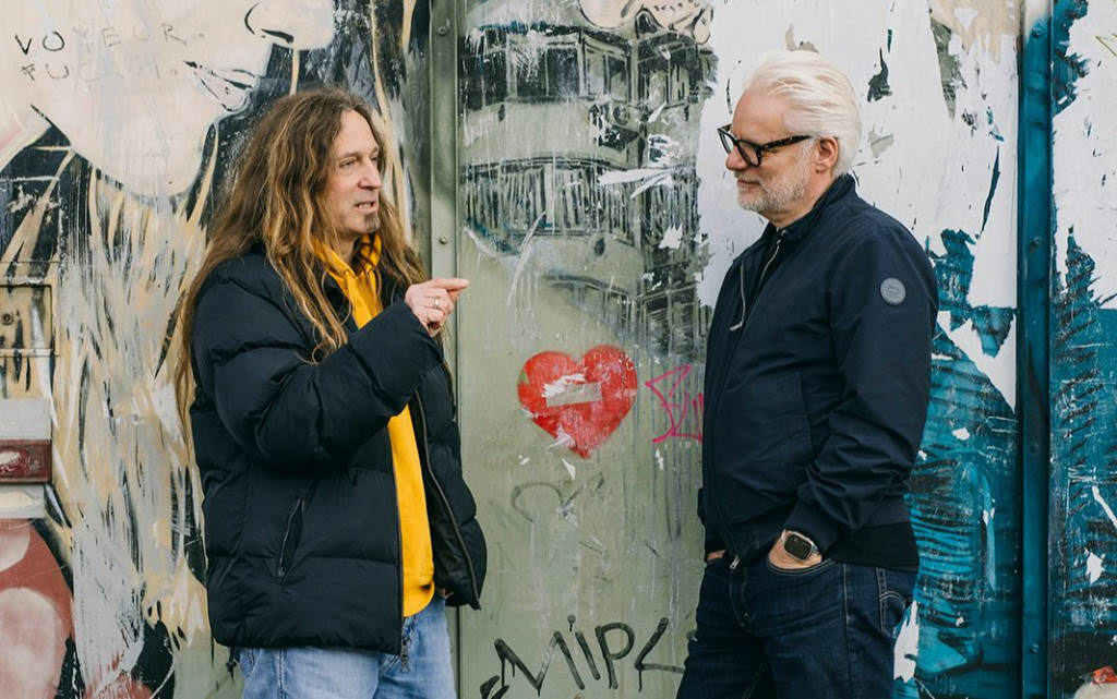 A photo in which you see two men in front of a graffiti from the side facing each other. One the left is Marc Thiele, on the right Rainer Kunst.