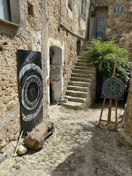The entrance of an artist studio in Bussana Vecchia with some art in fron of it on easels
