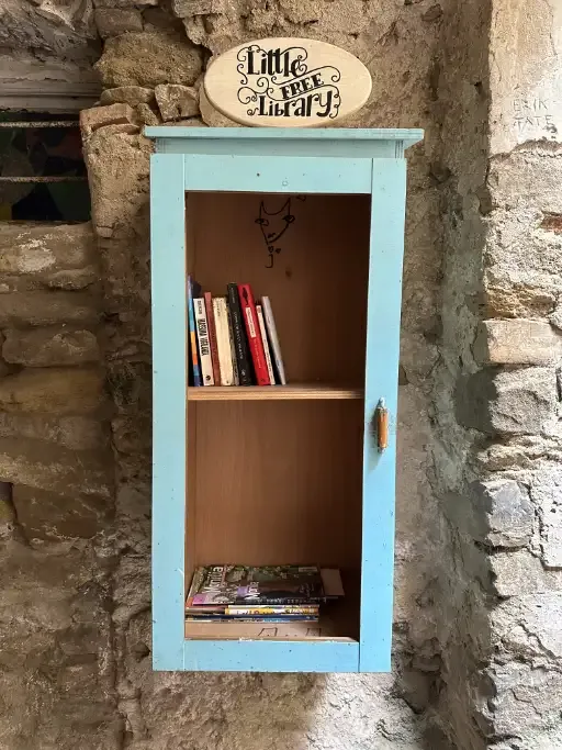 A small cupboard mounted to the old walls with a sign above stating “Little Free Library” and with books in it