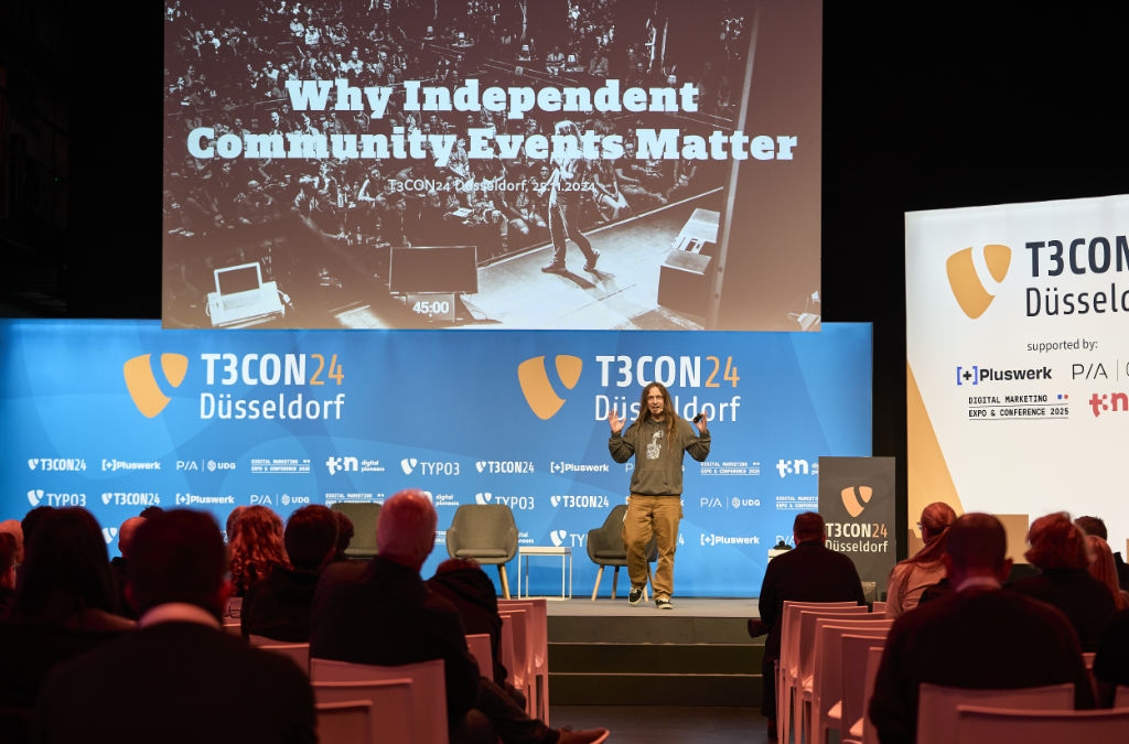 A photo of me on the stage at TYPO3 Conference. You can see the title slide stating “Why Independent Community Events Matter” and the audience sitting in front of the stage from the back.