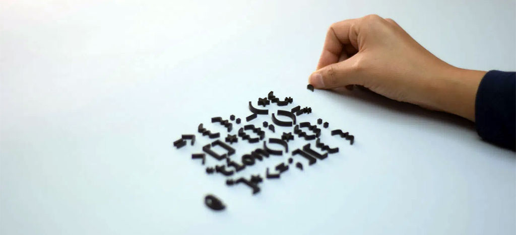 Photo showing a white background, with a hand of a women on the right, working with little signs and characters, laying them out on the white table