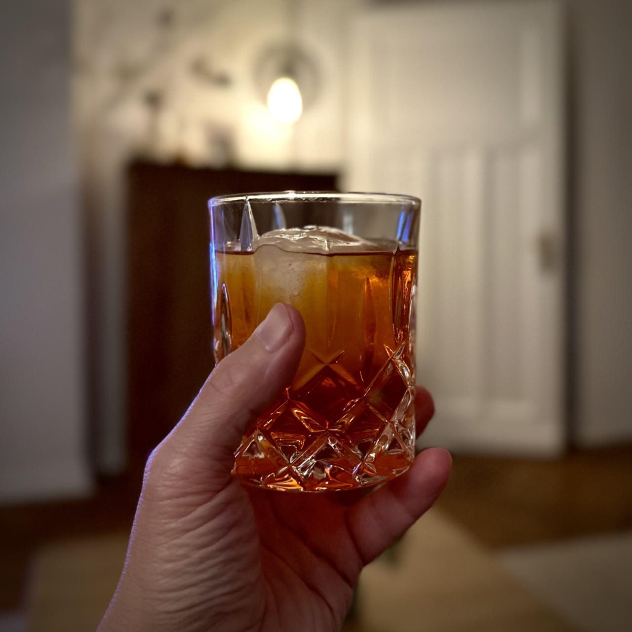 A squared photo on which you see my hand holding a negroni – a red drink containing equal parts of gin, sweet vermouth and Campari